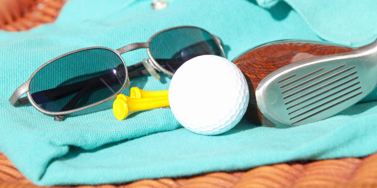 sunglasses, tees, golf ball, and clubs on top of a polo